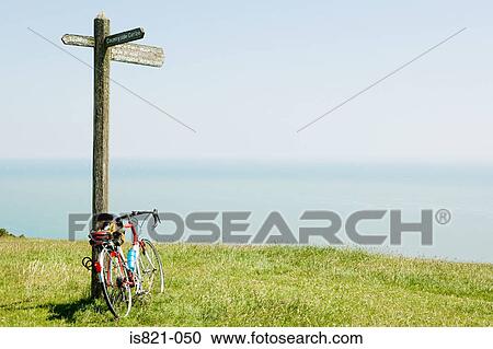 Stock Image - Bike leaning on a signpost by the sea. Fotosearch