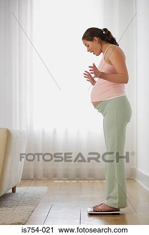 Stock Image - Pregnant woman on weight scales. Fotosearch