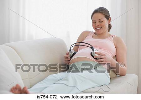 Stock Image - Pregnant woman with head phones on her stomach. Fotosearch