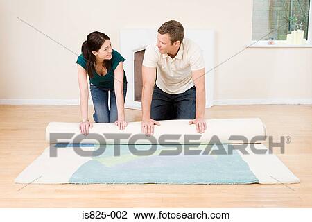 Stock Image - Couple rolling out rug. Fotosearch