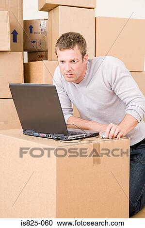Stock Image - Man using laptop on cardboard box. Fotosearch