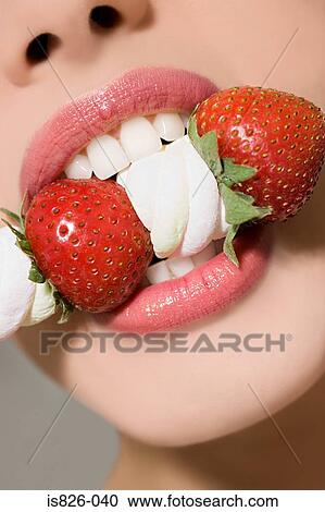 Stock Image - Woman biting strawberries and marshmallows. Fotosearch
