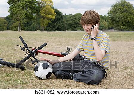 Stock Image - Teenage boy on cellphone in park. Fotosearch