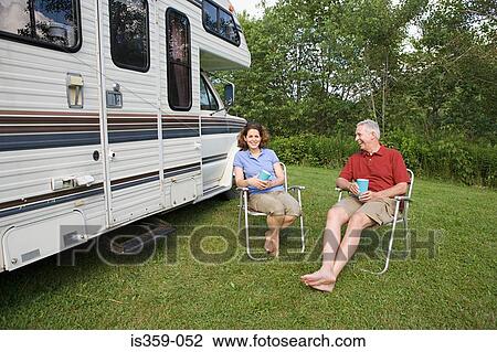Stock Image - Mature couple sitting near a caravan. Fotosearch