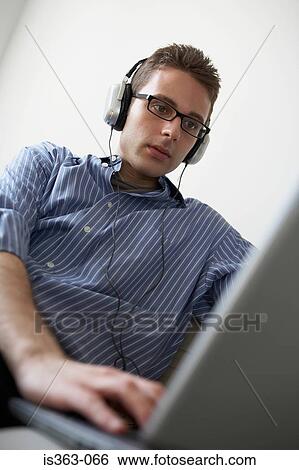 Stock Photograph - Man wearing headphones and using laptop. Fotosearch