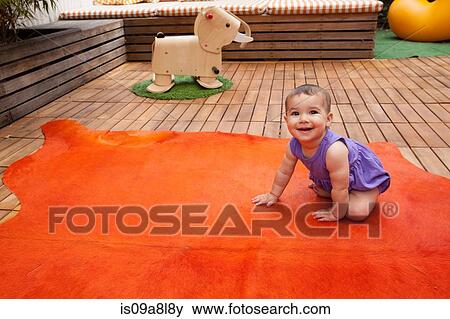 Stock Photo - Baby girl crawling on orange rug, portrait. Fotosearch