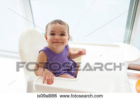Stock Photograph - Baby girl sitting in high chair smiling, portrait. Fotosearch