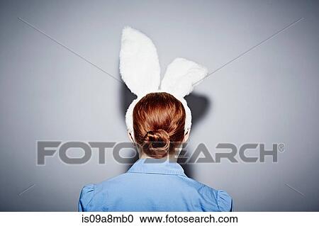 Stock Image - Back view of young woman wearing bunny ears. Fotosearch