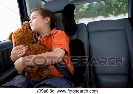 Stock Image - Boy looking out of car window holding teddy bear. Fotosearch