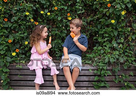 Brother and sister eating ice lollies by plants View Large Photo Image Picture - Brother and sister eating ice lollies by plants. Fotosearch