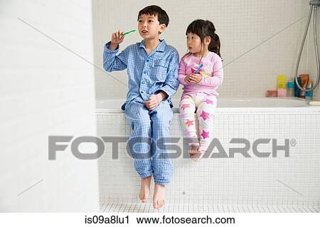 Stock Image - Brother and sister sitting on edge of bath with toothbrushes. Fotosearch