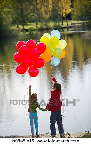 Stock Photography - Brother and sister with bunches of balloons in park. Fotosearch