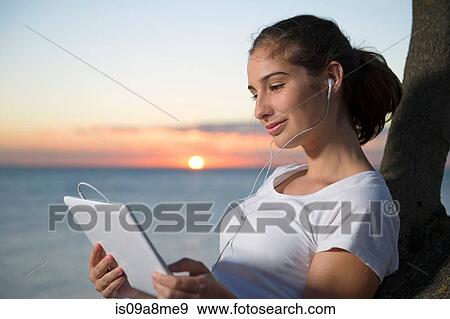 Close up of young woman looking at digital tablet at sunset View Large Photo Image Stock Photo - Close up of young woman looking at digital tablet at sunset. Fotosearch