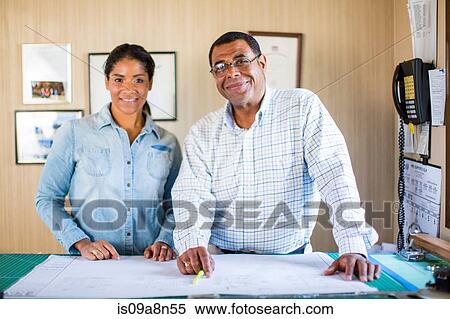 Stock Photography - Colleagues standing over blueprint in office. Fotosearch