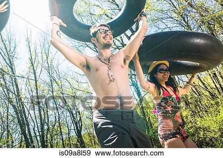Stock Photo - Couple carrying inner tubes above head. Fotosearch