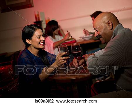 Stock Image - Couple enjoying wine in restaurant, smiling. Fotosearch