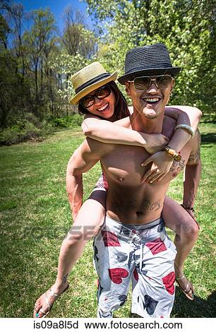 Stock Image - Couple in garden, man giving woman piggy back. Fotosearch