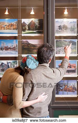 Couple looking at photographs in travel agents window, rear view View Large Photo Image Stock Photo - Couple looking at photographs in travel agents window, rear view. Fotosearch