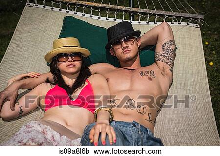 Stock Image - Couple wearing hats and sunglasses lying in hammock. Fotosearch