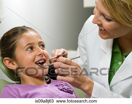 Stock Image - Dentist looking at young girl's teeth. Fotosearch