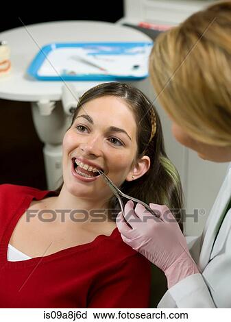 Stock Image - Dentist using dental pliers on young woman's braces. Fotosearch