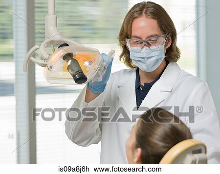 Stock Image - Dentist wearing face mask and using dental camera in examining room. Fotosearch