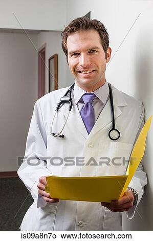 Picture - Doctor holding file in hospital corridor, portrait. Fotosearch