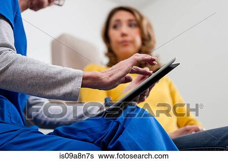 Stock Photograph - Doctor in blue scrubs using digital tablet with patient. Fotosearch
