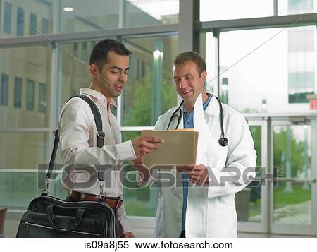 Doctor looking at file with mid adult man, smiling View Large Photo Image Stock Photography - Doctor looking at file with mid adult man, smiling. Fotosearch