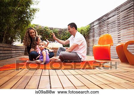 Stock Photo - Family sitting on rug on patio. Fotosearch