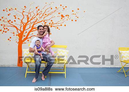 Stock Photograph - Father with two daughters in front of tree mural on wall. Fotosearch