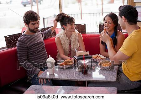 Stock Image - Four friends sitting together in diner, smiling. Fotosearch
