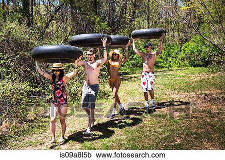 Stock Image - Four people carrying inner tubes above heads. Fotosearch