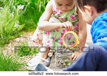 Girl and boy in garden watching jar of snails View Large Photo Image Stock Image - Girl and boy in garden watching jar of snails. Fotosearch