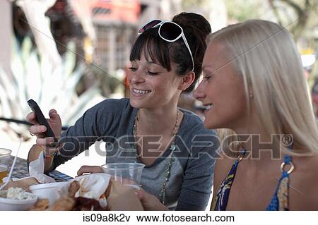 Girlfriends looking at mobile phone in outdoor cafe View Large Photo Image Stock Photo - Girlfriends looking at mobile phone in outdoor cafe. Fotosearch