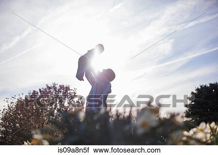 Stock Image - Grandfather holding up baby girl in garden. Fotosearch