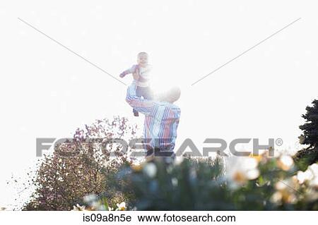 Stock Image - Grandfather lifting up baby girl in garden. Fotosearch