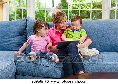 Stock Photography - Grandmother and grandchildren on sofa looking at digital tablet. Fotosearch