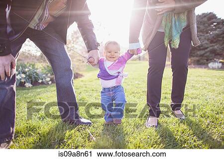 Stock Image - Grandparents walking granddaughter in park. Fotosearch