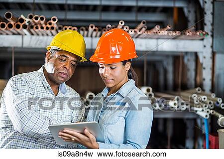 Man and woman in warehouse looking at digital tablet View Large Photo Image Stock Photo - Man and woman in warehouse looking at digital tablet. Fotosearch