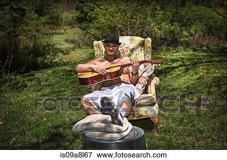 Man playing guitar sitting in armchair in garden View Large Photo Image Stock Photo - Man playing guitar sitting in armchair in garden. Fotosearch