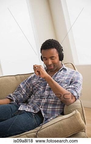 Man wearing headphones listening to music on sofa View Large Photo Image Stock Photo - Man wearing headphones listening to music on sofa. Fotosearch
