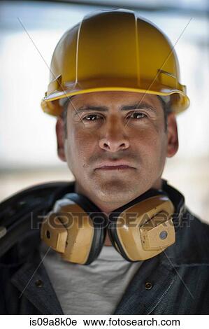 Stock Image - Mature construction worker wearing hard hat and ear defenders. Fotosearch