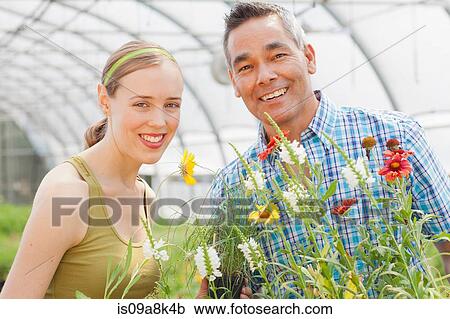 Stock Image - Mature man and mid adult woman shopping in garden centre, smiling. Fotosearch