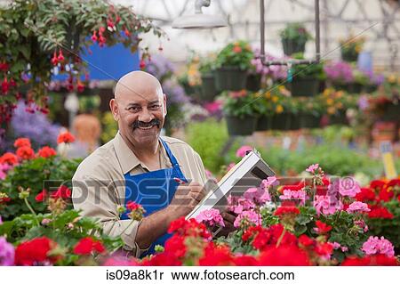 Stock Photography - Mature man using clipboard in garden centre, portrait. Fotosearch