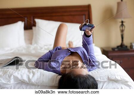 Mature woman lying on bed and listening to mp3 player View Large Photo Image Picture - Mature woman lying on bed and listening to mp3 player. Fotosearch