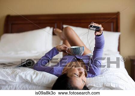 Picture - Mature woman lying on bed and listening to mp3 player, smiling. Fotosearch