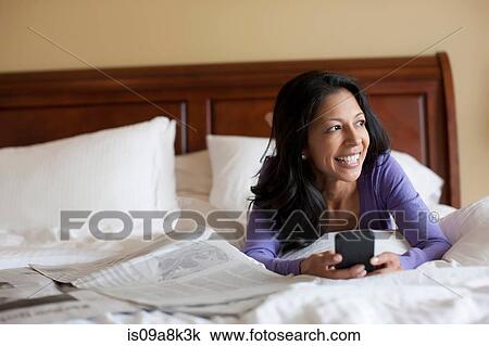 Mature woman lying on bed holding mobile phone, smiling View Large Photo Image Stock Image - Mature woman lying on bed holding mobile phone, smiling. Fotosearch