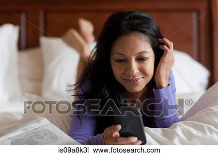 Mature woman lying on bed looking at mobile phone, smiling View Large Photo Image Stock Image - Mature woman lying on bed looking at mobile phone, smiling. Fotosearch