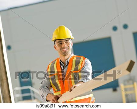 Mid adult construction worker holding wood View Large Photo Image Stock Image - Mid adult construction worker holding wood. Fotosearch